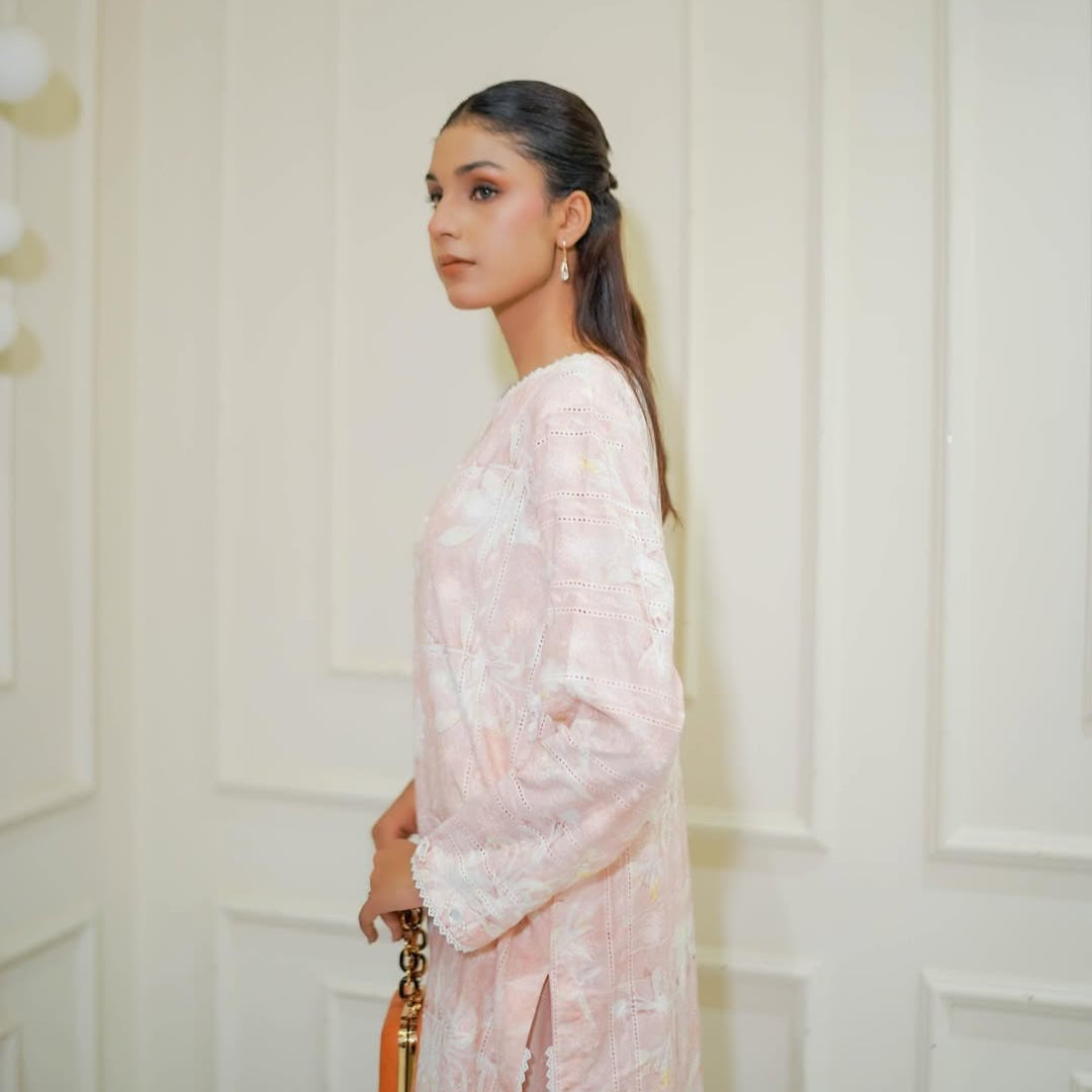 Woman in a light pink floral dress standing against a white paneled wall.