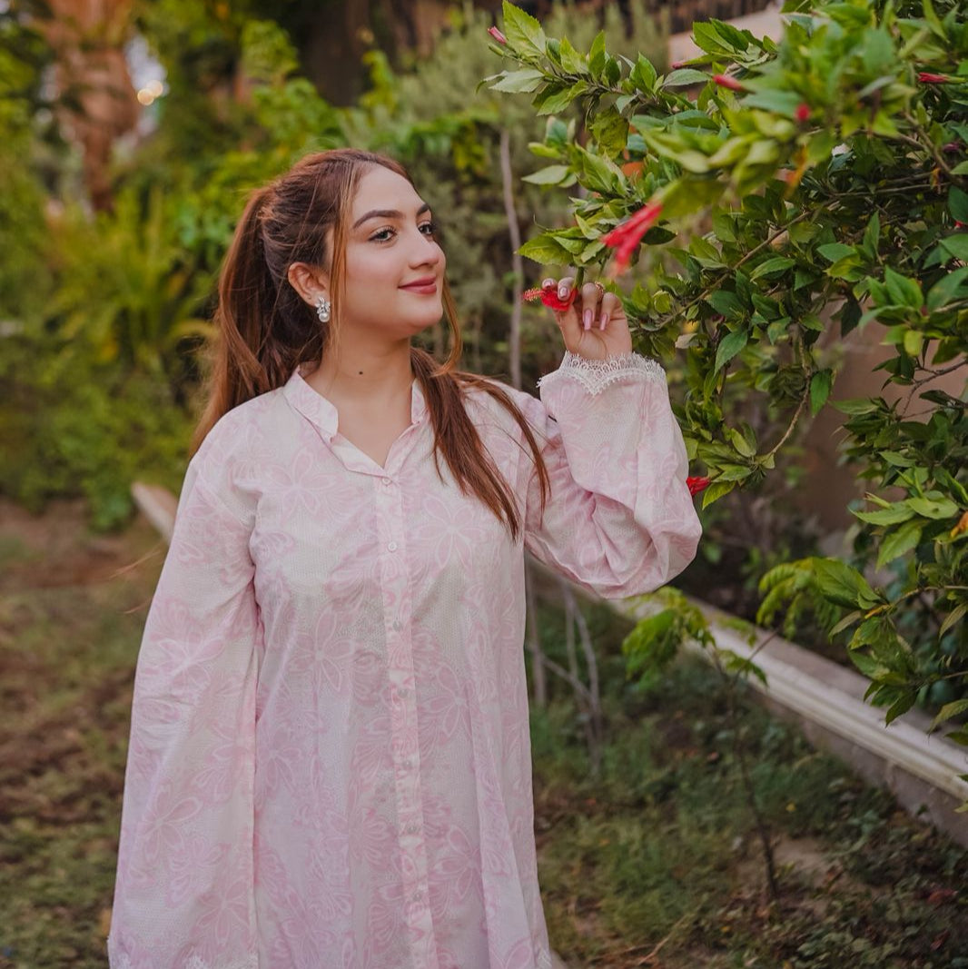 Woman in a pink dress standing in a garden with greenery and flowers.